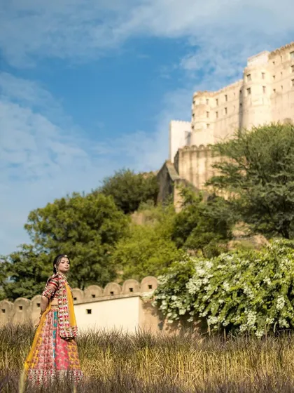 A wide shot of the bride in her colorful Mehendi lehenga against the backdrop of a majestic fort. This image highlights both the stunning outfit and the epic destination.