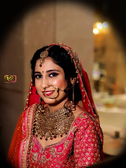 A classic bridal portrait with a soft, dreamy edit. The focus is on the bride's happy expression and the intricate details of her jewelry and lehenga.