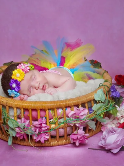 A one-month-old baby girl in a rainbow tutu, sleeping in a basket decorated with flowers.