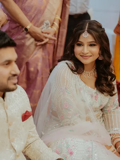 A candid moment from an engagement ceremony. The bride's soft airbrush makeup in pink tones complements her beautiful white and pink lehenga.