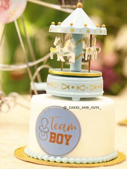 A close-up of the "Team Boy" mini cake with a blue carousel topper, part of a larger dessert table.