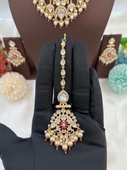 The 'Ziva' premium maang tikka, featuring a floral motif with red stones and pearls.
