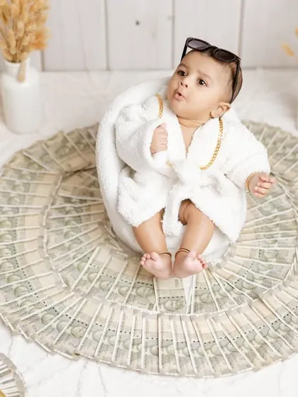 A wide shot of the 'Royal Karbhar' setup, showing the baby sitting on a rug made of money, surrounded by props.