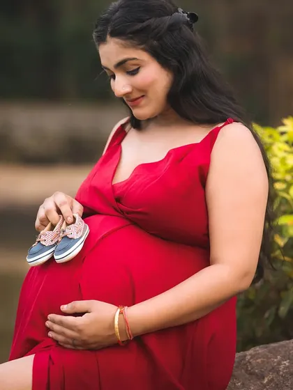 A sweet and symbolic outdoor maternity photo. The mother-to-be holds a tiny pair of baby shoes against her bump, signifying the new life to come.