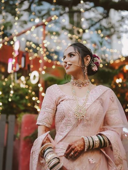 The bride against a backdrop of festive lights. Her soft makeup and floral bun create a romantic and ethereal vibe.
