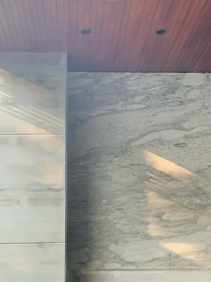 The intersection of materials: a wooden ceiling meets a stone-clad wall, with a glass panel creating a subtle reflection. This careful detailing is where the tectonic quality of the architecture is expressed.