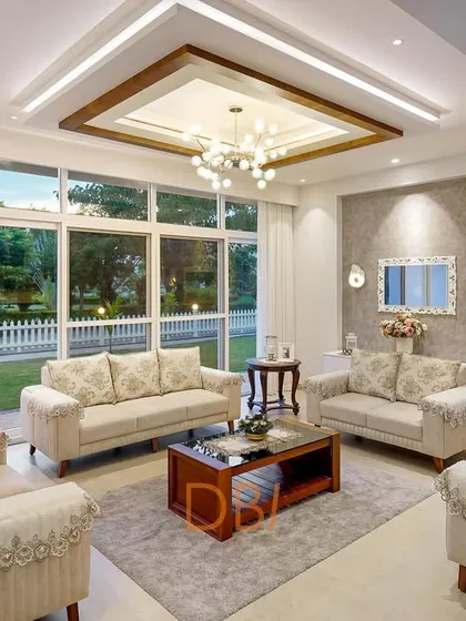 A bright and welcoming living room with large windows that look out onto a green garden. The classic sofa arrangement and warm, neutral tones create a comfortable yet elegant space, perfect for family gatherings.