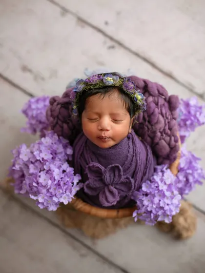 A lovely purple-themed setup. The baby is wrapped snugly in a basket with matching purple flowers, creating a rich and colorful portrait.