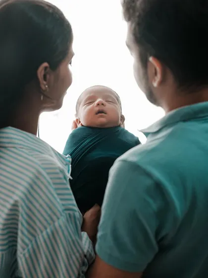 A unique over-the-shoulder perspective as both parents gaze down at their newborn. This shot emphasizes the baby as the center of their world.