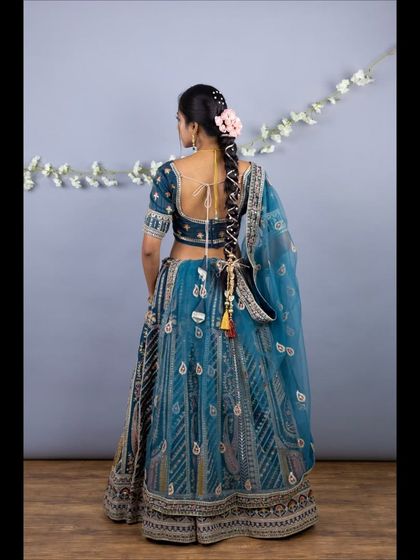 The back view of the teal lehenga, showing the stylish blouse back and the colorful tassels on the skirt.