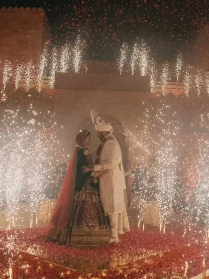 A wide shot capturing the sheer scale of the celebration, with the couple at the center of a dazzling cold pyro display against the magnificent backdrop of Suryagarh fort. It's a moment of pure, unadulterated magic.
