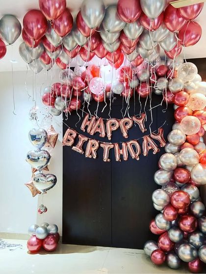 This full-doorway balloon decoration creates a grand entrance for a birthday party. The design uses rose gold and silver balloons, with 'Happy Birthday' foil letters as the centerpiece.