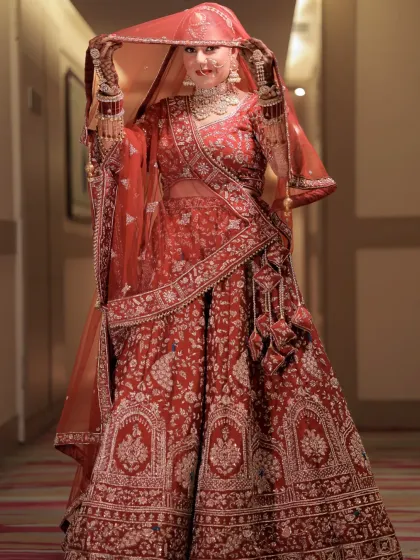 A classic bridal portrait. The bride, in her traditional red lehenga, lifts her veil, her confident smile capturing the essence of modern royalty.