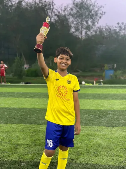 A player confidently holds his trophy high, celebrating a significant achievement in his football journey.