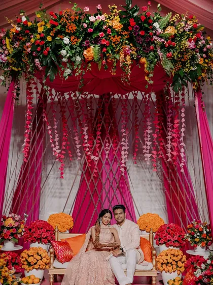 A beautiful couple framed by our vibrant Mehendi decor. The design features a canopy of lush, colorful flowers and a unique lattice backdrop, creating an intimate and joyful setting that is rich in color and texture.