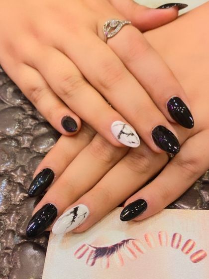 A classic and chic design on almond-shaped nails. The glossy black polish is paired with accent nails featuring a white marble effect.