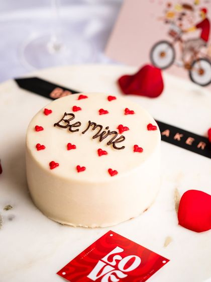 A "Be mine" bento cake surrounded by rose petals. These little cakes are designed for intimate moments and thoughtful gestures.