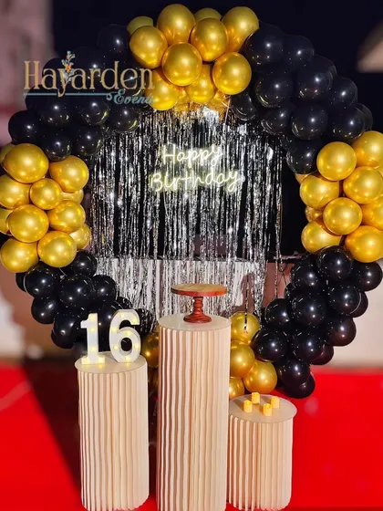 A classic black and gold sweet 16 party. The circular balloon frame, silver fringe backdrop, and marquee numbers create a festive and grown-up party look.