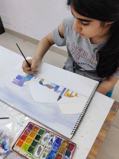 A teen student works on a scenic watercolor landscape, learning to create depth and atmosphere with washes of color.