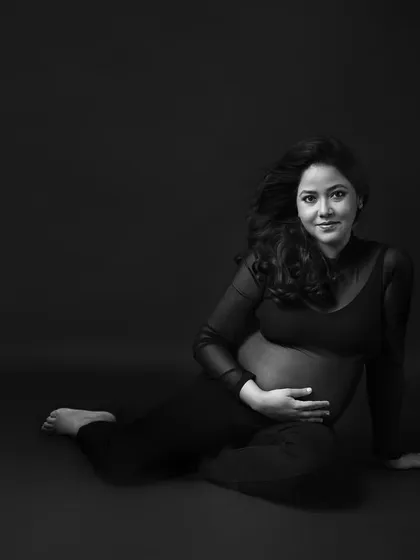 A simple, elegant seated portrait. In black and white, the focus is entirely on her serene expression and the beautiful shape of her bump.