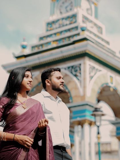 A couple in traditional wear looks towards the future, with a historic clock tower in the background, symbolizing their timeless love.