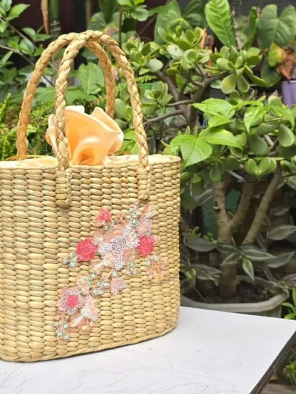 This beautifully crafted tote bag, made from woven water hyacinth, features delicate pink floral beadwork and a soft cloth interior. It's a perfect example of how we blend traditional weaving techniques with contemporary design for a truly unique accessory.