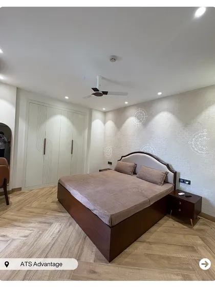 A serene bedroom with herringbone wooden flooring and full-height white wardrobes that provide ample storage. The subtle stencil work on the wall adds a touch of traditional elegance.