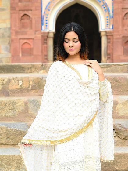 An elegant portrait of a model in a white ethnic suit, shot outdoors against a historical backdrop.