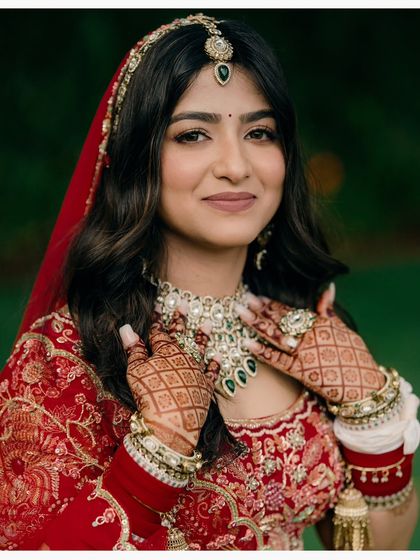 A classic bridal portrait focusing on the bride's beauty and intricate details. Her gentle smile, mehendi-adorned hands, and stunning jewelry are all highlighted.