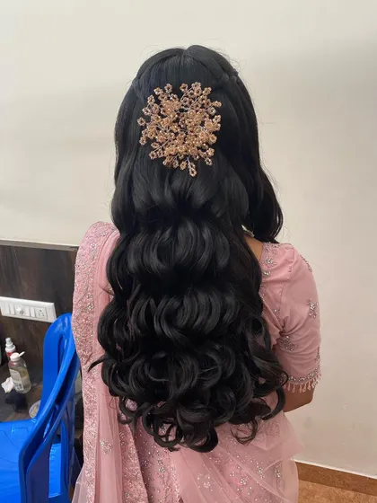 A glamorous half-updo with voluminous waves and a large, sparkling gold hair accessory.