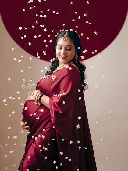 A serene portrait of the mother to be, cradling her bump. The falling petals around her create a magical atmosphere, highlighting the miracle of the moment.