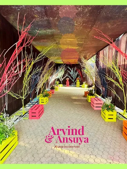 A colorful and creative entrance for a neon Haldi party. The walkway is lined with painted tree branches and colorful crates, creating a vibrant and artistic welcome.