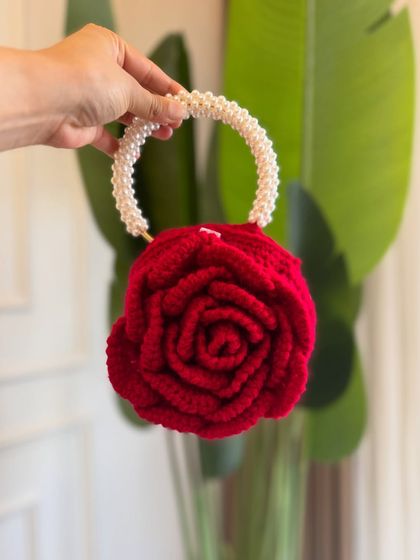 A close-up of the red Peony Bag, showing the detailed rose-like construction and the elegant pearl handle.