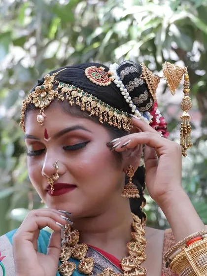 Adjusting the hairpiece, this shot shows the beautiful contrast between the gold jewelry and the vibrant saree.