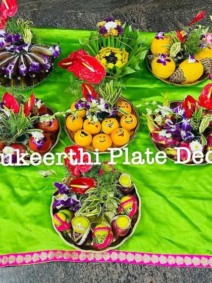 An assortment of decorated platters showcasing different styles. You can see arrangements with fresh flowers like anthuriums, fruits like apples and oranges with smiley faces, and beautifully wrapped sweets.