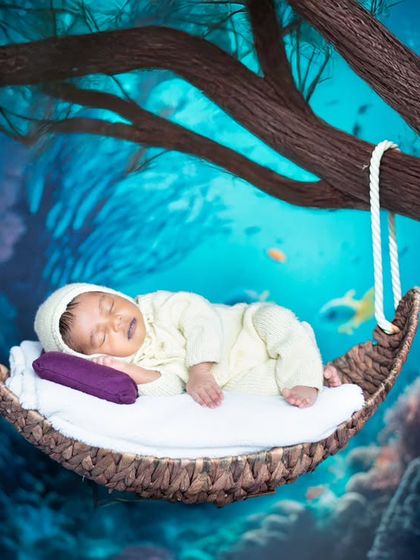 A magical underwater dream. This newborn is sleeping in a swing hanging from a tree, with a beautiful coral reef in the background.