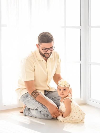 A father and his six-month-old daughter share a moment by the window. The soft natural light illuminates this tender interaction, creating a beautiful and gentle portrait.
