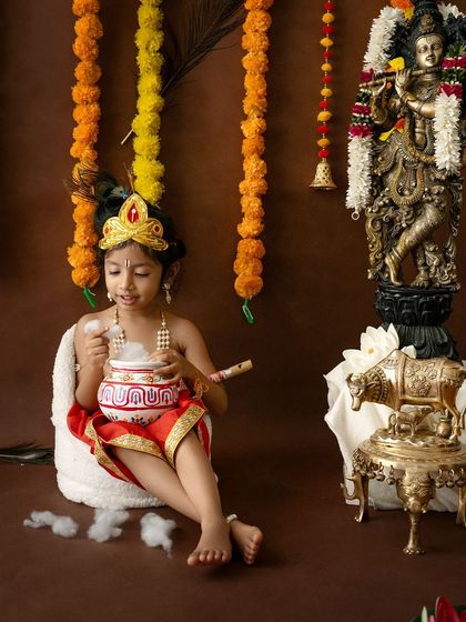 A solo shot of an older child dressed as Krishna, enjoying a pot of butter in a simple, traditional setting.