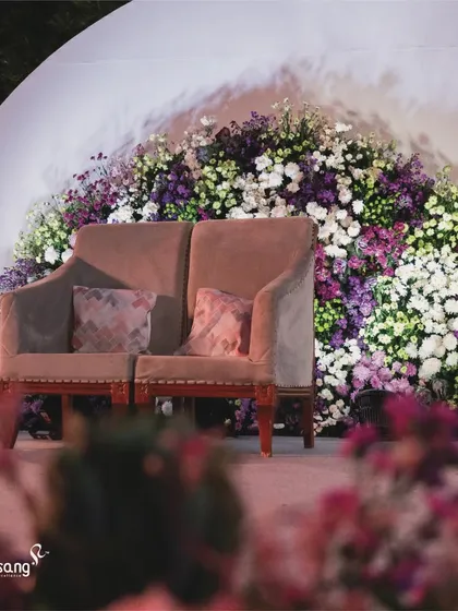 A beautifully designed stage with a backdrop of cascading flowers. The seating is arranged to be both comfortable for the couple and aesthetically pleasing for photos.