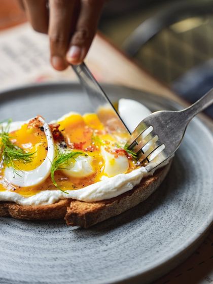 The perfect egg yolk moment. A knife and fork cut into a soft-boiled egg on our Turkish toast, with the yolk ready to run.