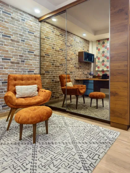The den at Rue 32, a versatile space reimagined from a walk-in closet. It combines a home office, reading nook, and storage, featuring a cantilevered workstation, exposed brick, and a comfortable lounge chair to create a handcrafted masterpiece of space and solace.