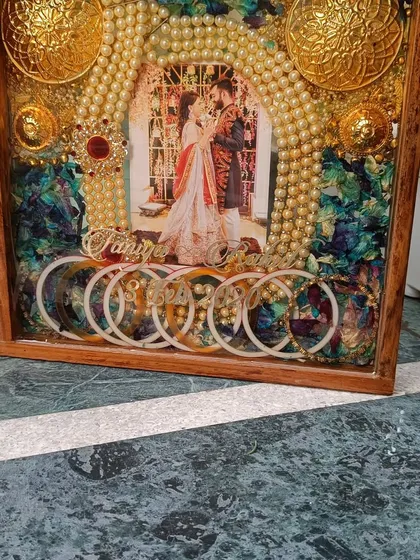 A side view of a custom wedding ornament frame. This piece includes preserved orchid flowers, kaleere, chooda, and a pearl mala, all encased in a beautiful wooden box frame.