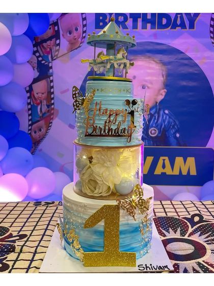 A 3kg Dutch truffle cake for a first birthday. This spacer cake features a rotating carousel on top and is decorated in a blue and white theme with golden butterflies.