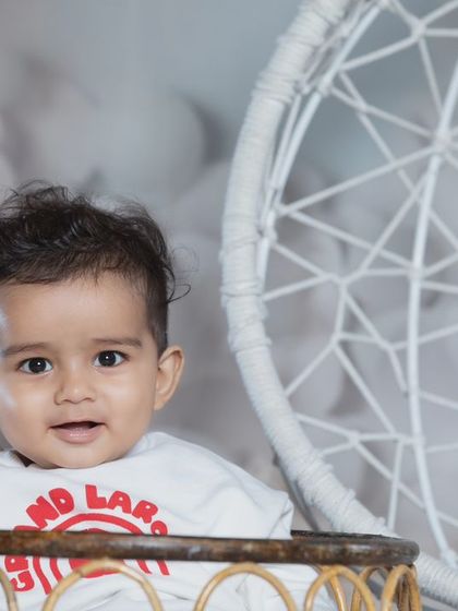 A curious little boy with stylish hair, posing in a basket with a dreamcatcher in the background.