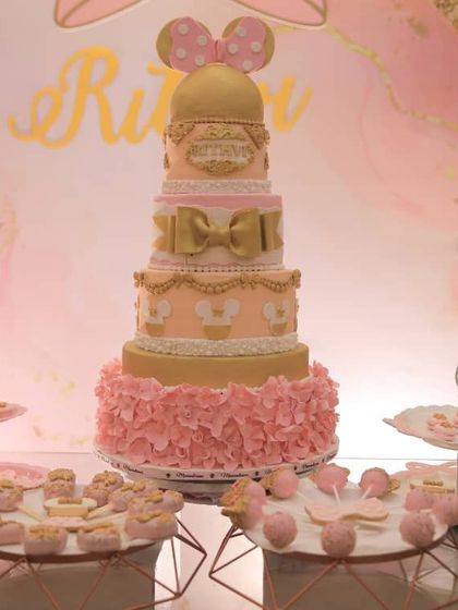 A full view of the stunning dessert table for a Minnie Mouse themed first birthday. The grand five-tiered cake is surrounded by perfectly coordinated cookies, cake pops, and other treats.