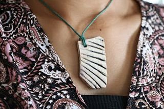A close-up of a handmade ceramic pendant with a carved line pattern, worn on a simple cord. It's a statement piece that is both modern and earthy.