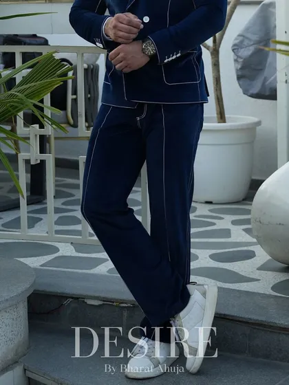 A detail of the blue velvet trousers, showing the continuation of the white piping and the perfect break over the crisp white sneakers.