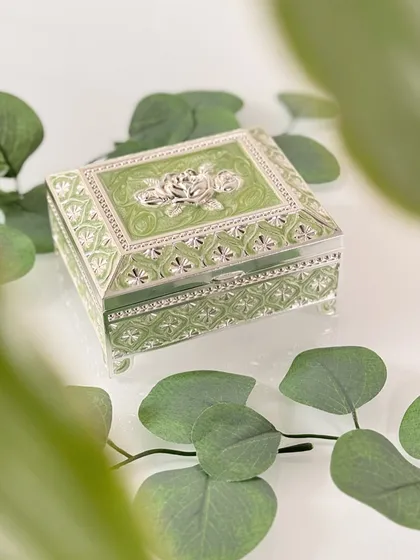A pastel green enamel box with silver rose detailing and a plush velvet interior. This piece is made for precious items and quiet moments, looking as beautiful on your dresser as what it holds inside.