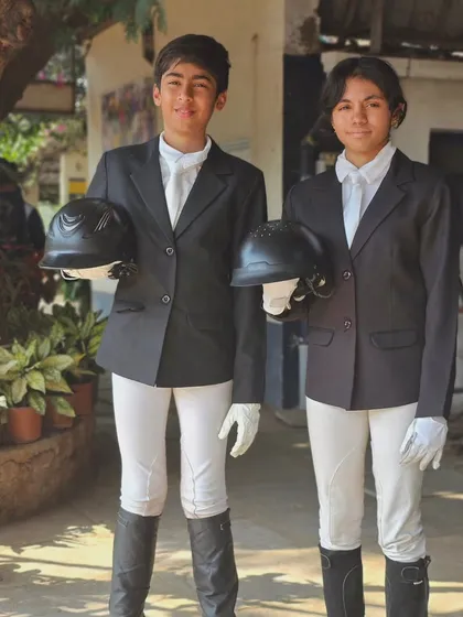Two young riders in their formal show attire, holding their helmets. This captures the sense of pride and professionalism we foster in our equestrian team.