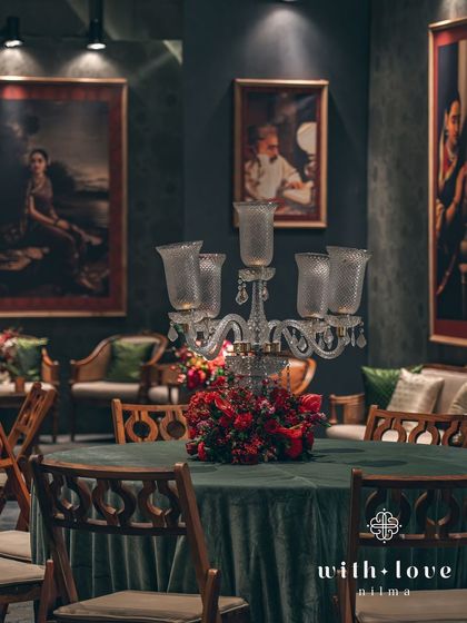 A wide view of the guest seating, with tables draped in green velvet and topped with candelabras. The entire room is bathed in warm, dramatic light, echoing the chiaroscuro effect in Varma's paintings.
